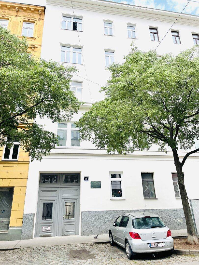 Weiße Gebäudefassade mit klassischen Fenstern und einem geparkten Auto davor an der Straße.