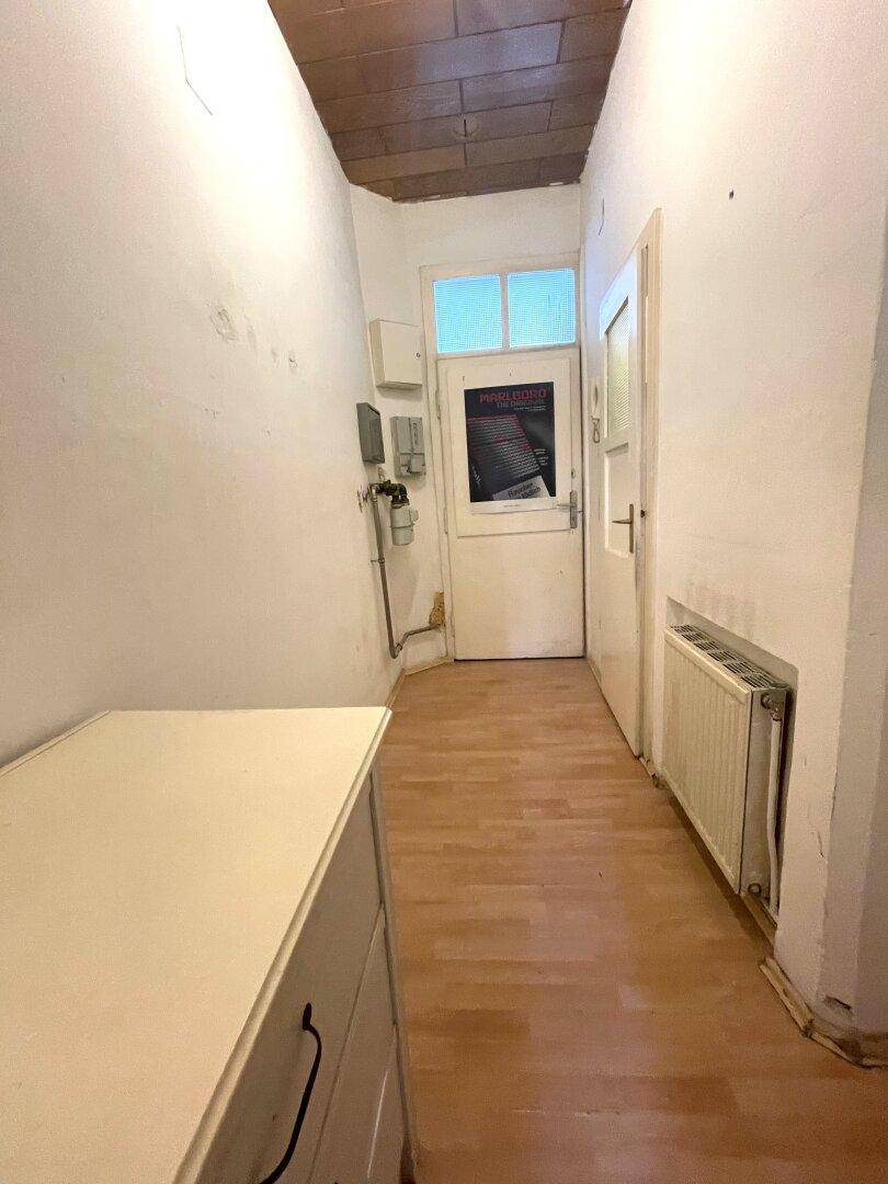 Schmaler Flur mit Holzfußboden und Heizkörper, führt zu weiteren Räumen im Apartment.