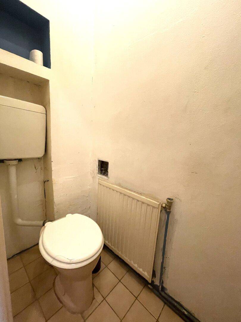 Kleines WC mit Fliesenboden und Heizkörper, bietet grundlegende Sanitäranlagen im Badbereich.