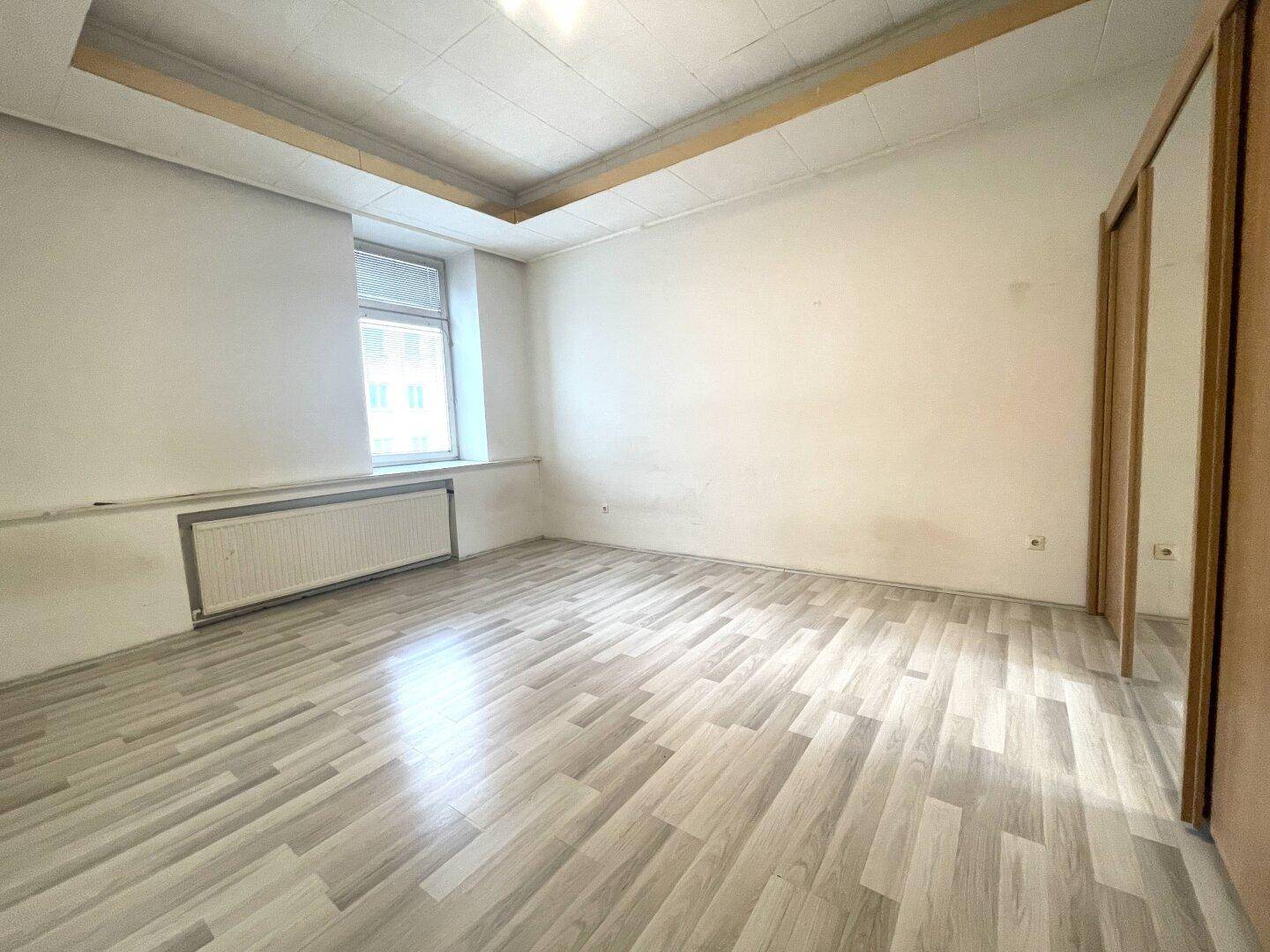 Helles, leeres Zimmer mit Laminatboden und einem Fenster, bereit zur individuellen Gestaltung.