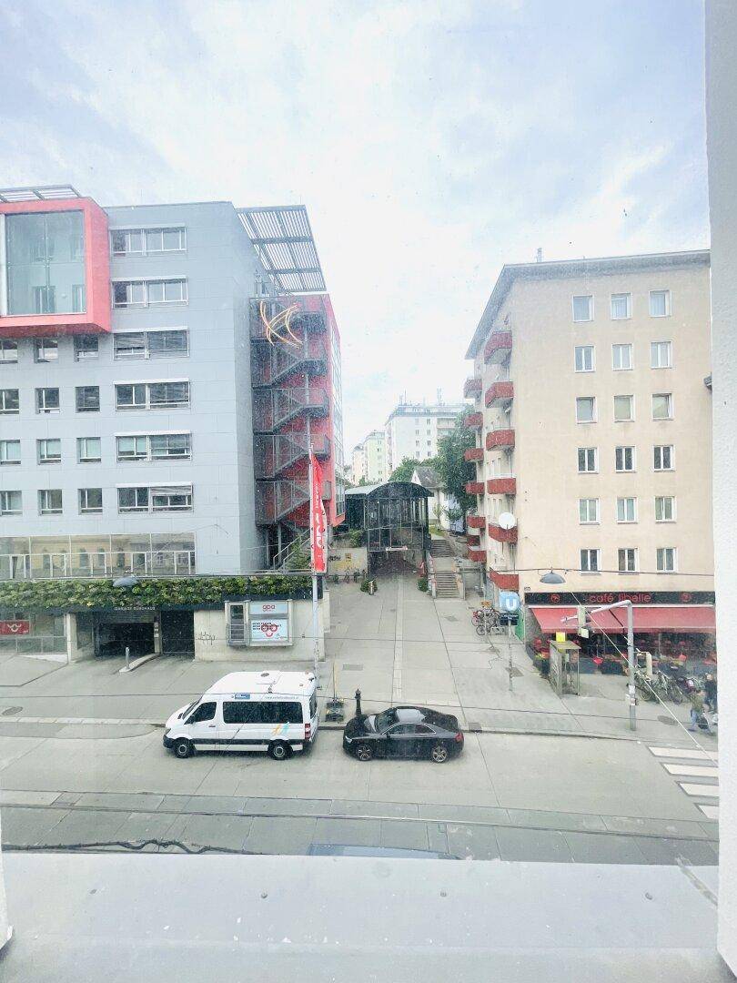Blick aus dem Fenster auf eine belebte Stadtstraße mit modernen und klassischen Gebäuden.