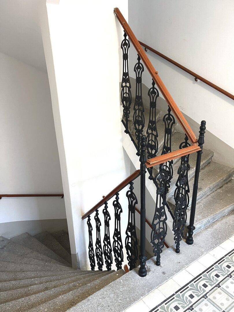 Detailansicht einer historischen Treppe mit schmiedeeisernem Geländer und Holzhandlauf.
