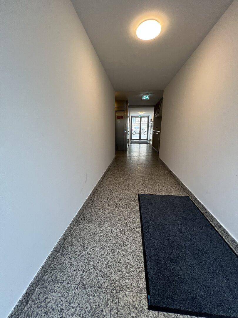Langer, heller Flur im Gemeinschaftsbereich mit Fliesenboden und Ausgang zum Freien.