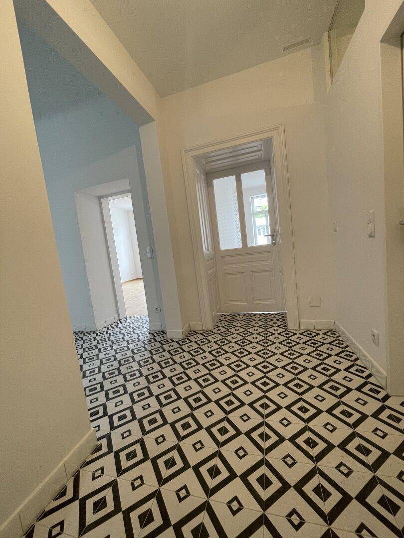 Eingangsbereich mit markantem schwarz-weißem Fliesenboden und einer klassischen Tür mit Glaseinsätzen.