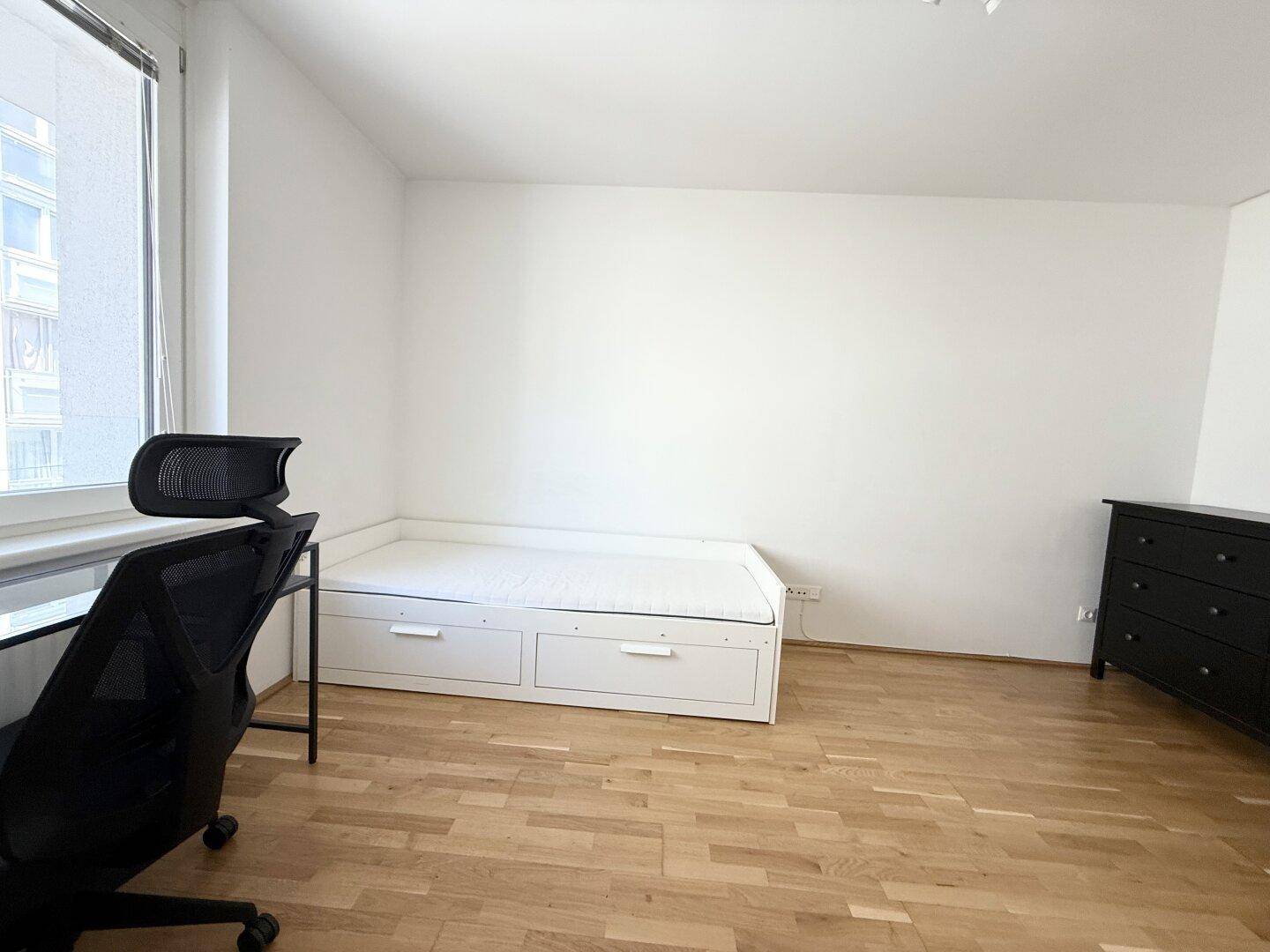 Funktionales Schlafzimmer mit Tagesbett und integrierten Schubladen sowie einem dunklen Sideboard.