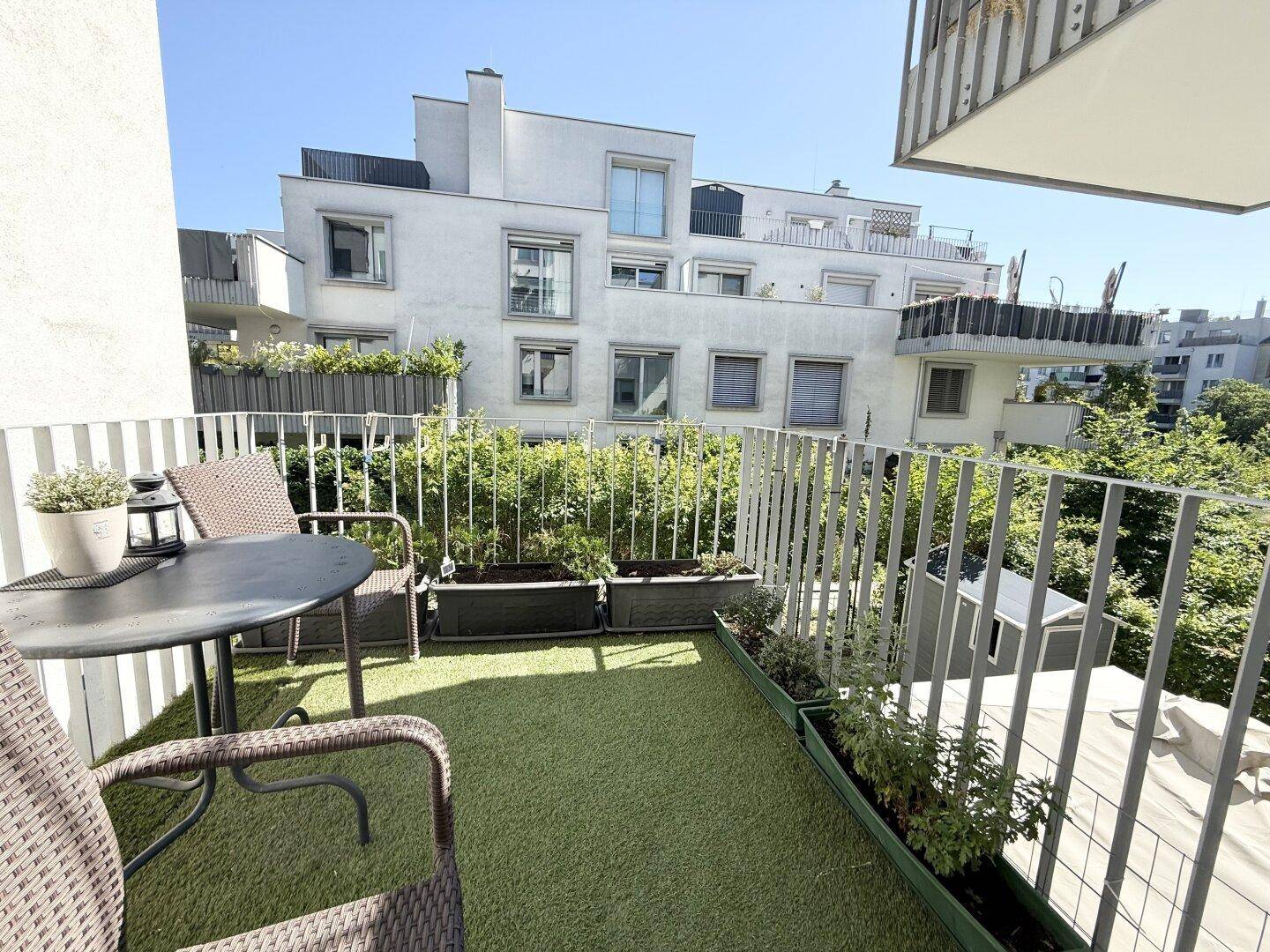 Sonniger Balkon mit Kunstrasen, bequemen Sitzgelegenheiten und Blick auf die umliegende Wohnbebauung.