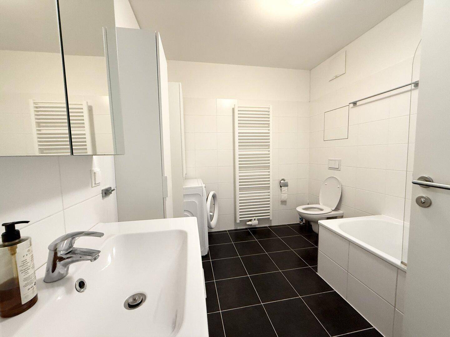 Geräumiges Badezimmer mit Badewanne, WC, Waschbecken, Waschmaschine und Handtuchheizkörper.