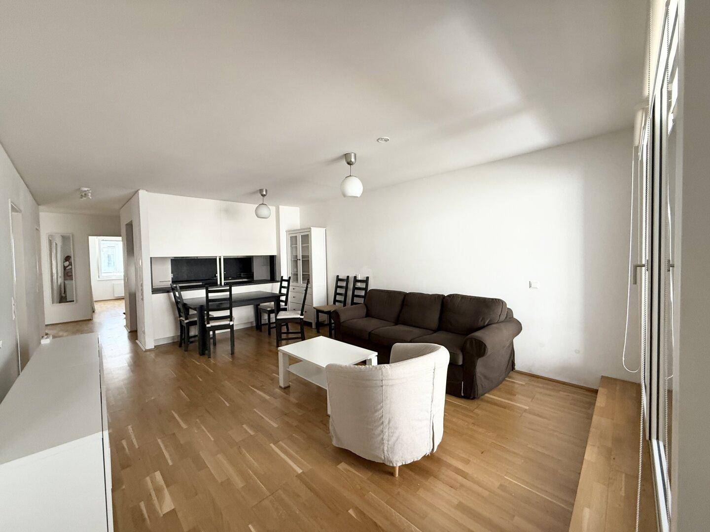 Geräumiger Wohn-Essbereich mit hellem Parkettboden, bequemer Couch und modernem Essbereich.