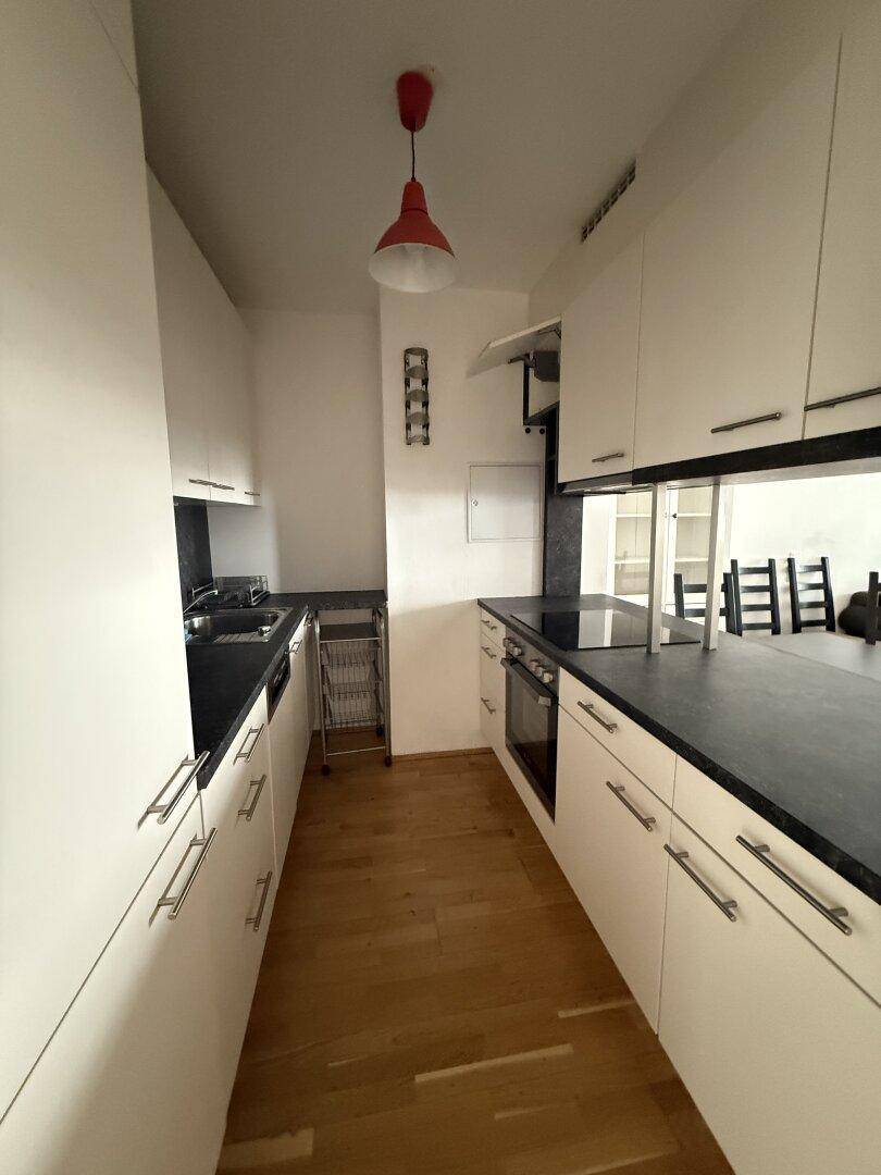Moderne Küchenzeile mit weißen Schränken, dunklen Arbeitsplatten und integriertem Backofen.