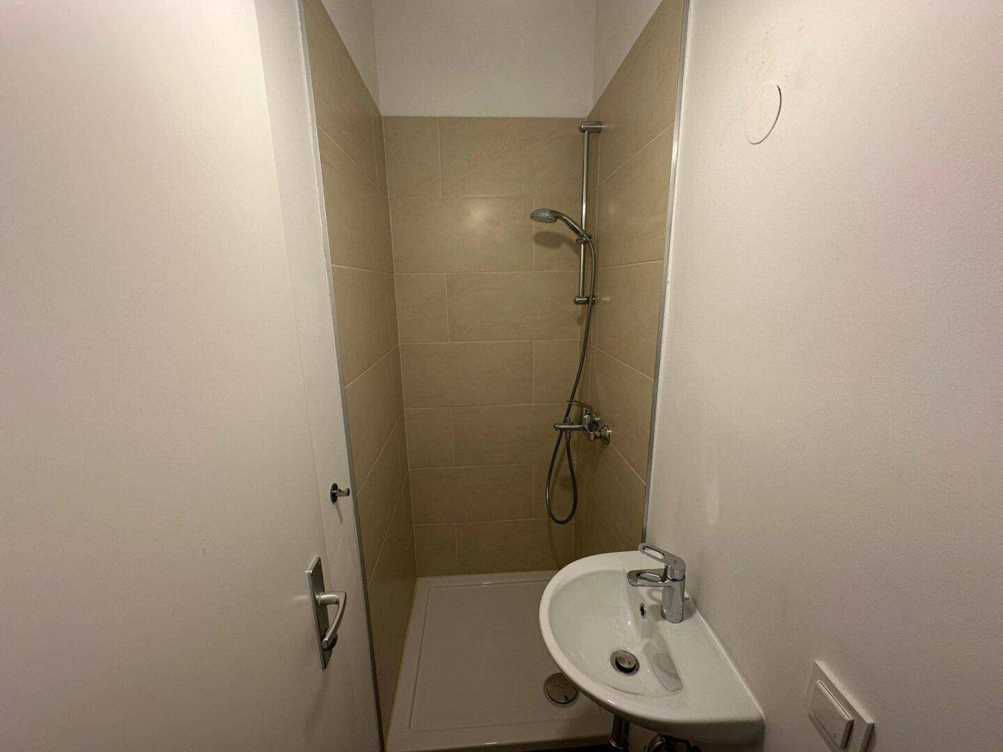 Kleines Badezimmer mit Duschbereich und Waschbecken in hellen Fliesen, funktional und sauber.