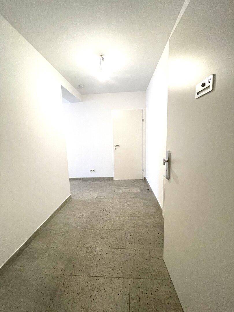 Heller Flur mit grauen Fliesen, weißen Wänden und einer modernen Eingangstür.