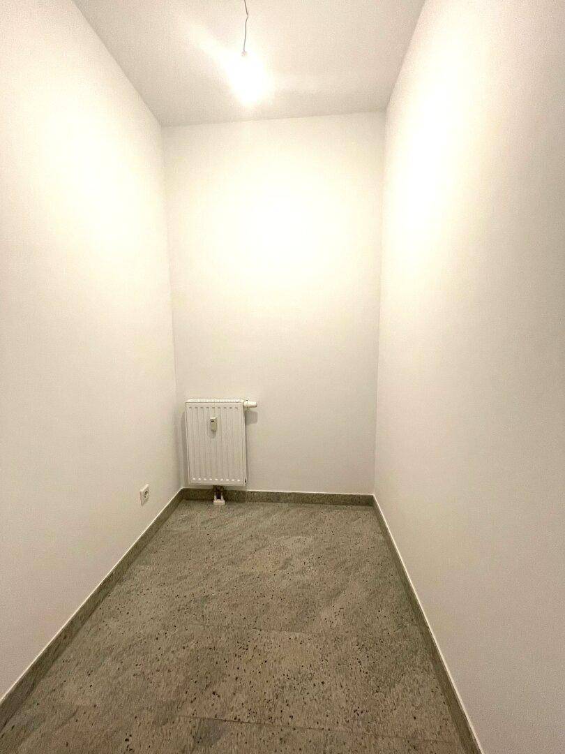 Kleiner, leerer Raum mit Fliesenboden, weißen Wänden und einem Heizkörper, ideal als Abstellraum.