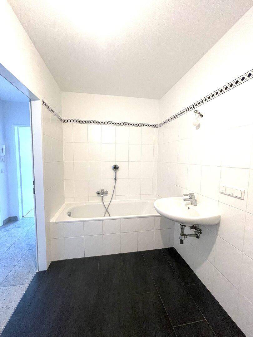 Badezimmer mit Badewanne, Waschbecken, weißen Fliesen und einem dekorativen Bordürenband.