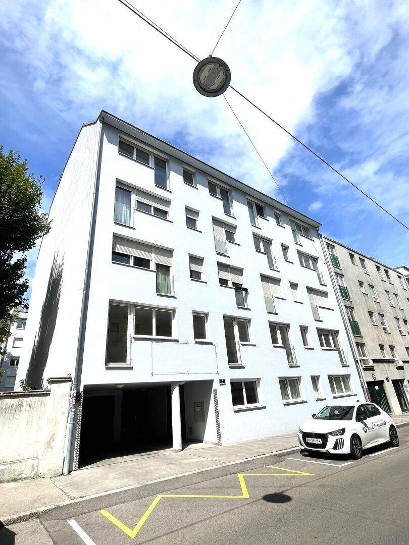 Weißes Wohngebäude mit Tiefgarageneinfahrt und einem geparkten Auto an der Straße.