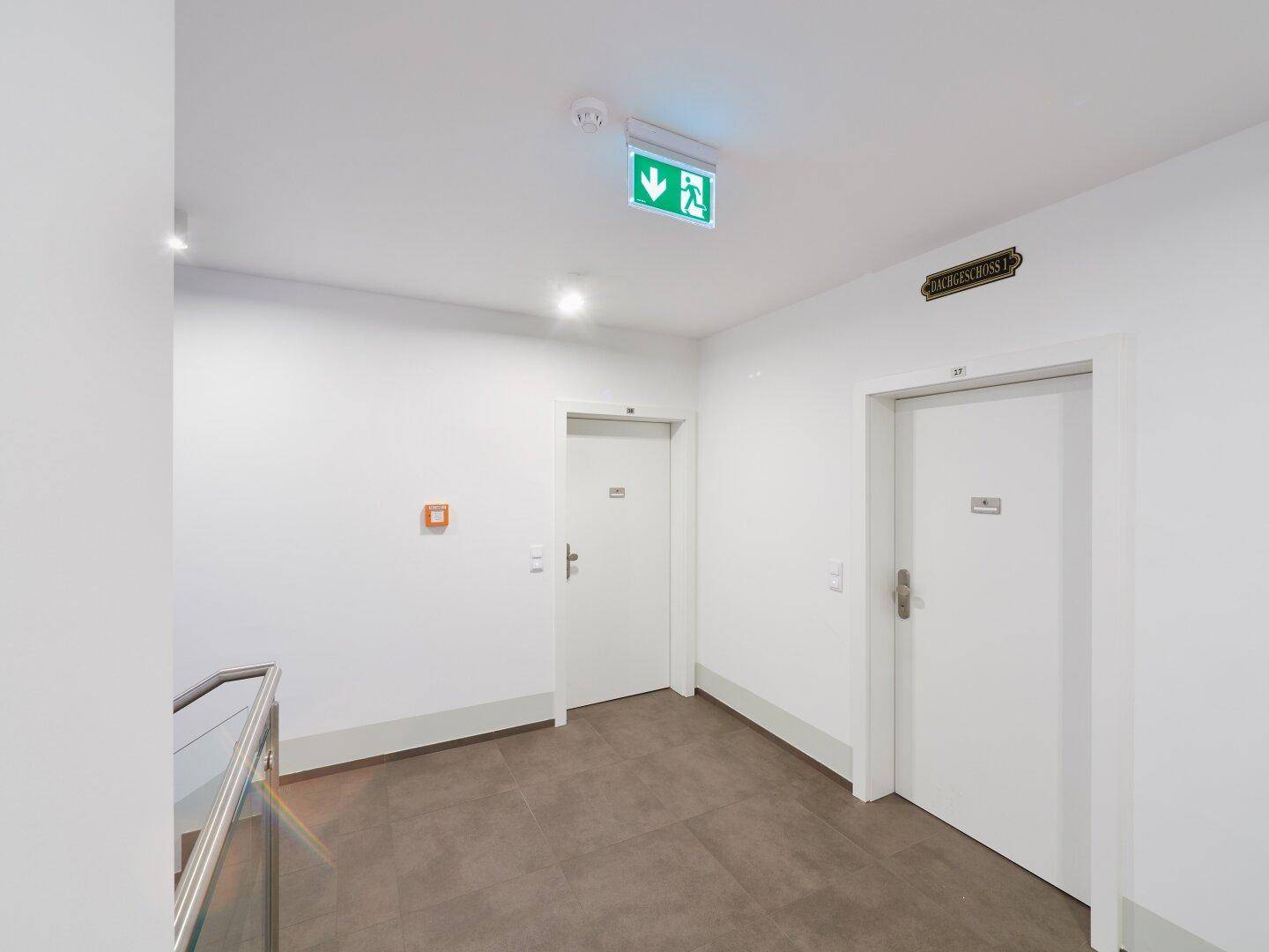 Moderner und heller Flur mit weißen Wänden, dunklen Fliesen und Wohnungstüren.