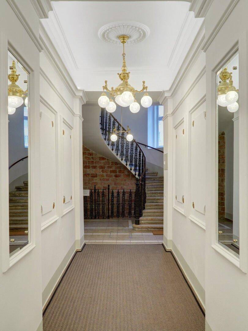 Eleganter Flur mit hohen Decken, Stuckverzierung und einem prächtigen Kronleuchter, der zu einer geschwungenen Treppe führt.