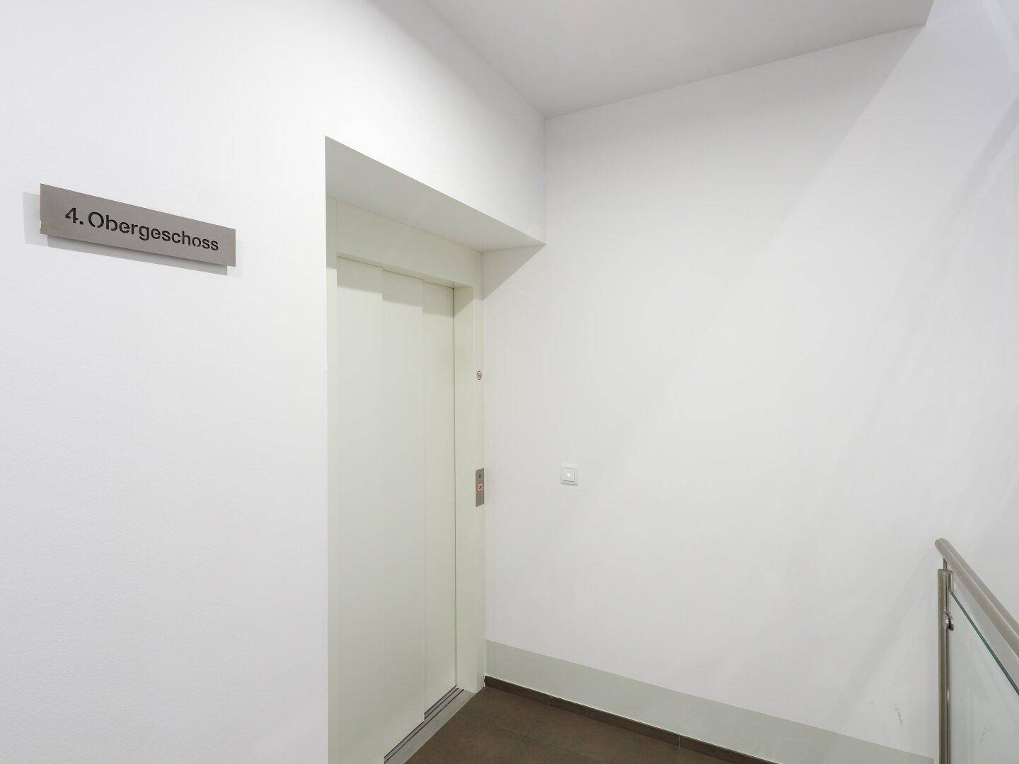 Heller Flur im vierten Obergeschoss mit modernem Aufzug und weiß gestrichenen Wänden.