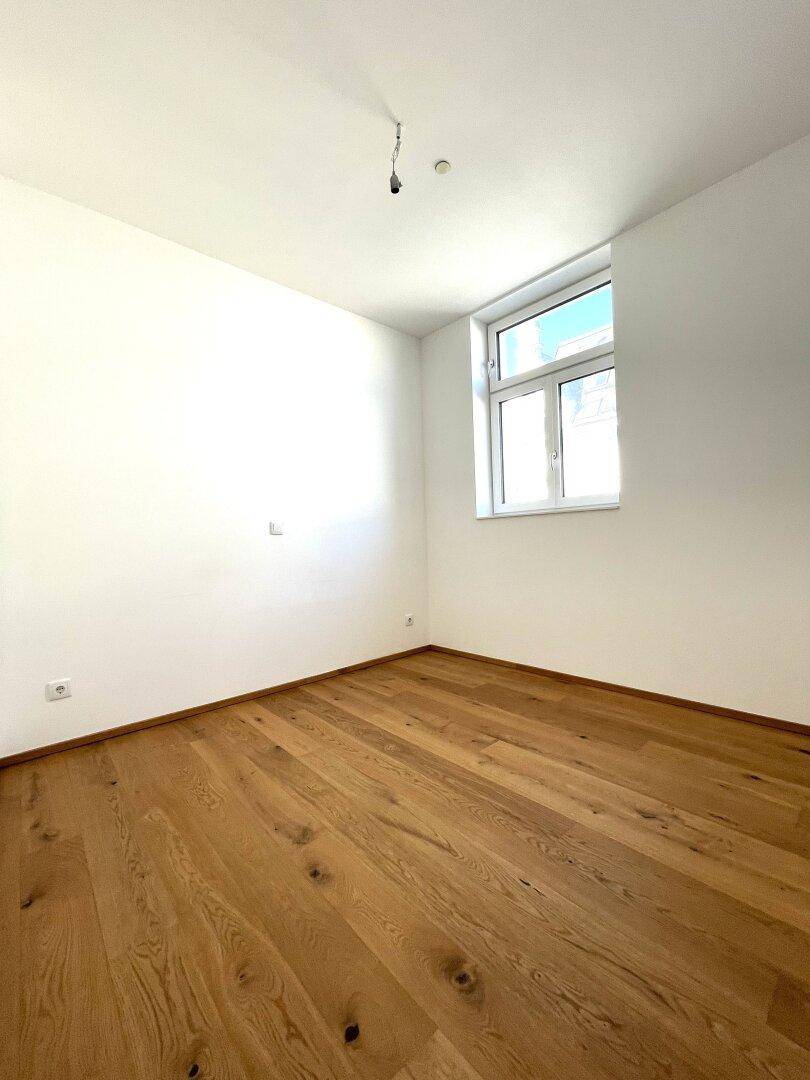 Geräumiges Zimmer mit hellem Holzfußboden und einem Fenster, bereit zur individuellen Gestaltung.