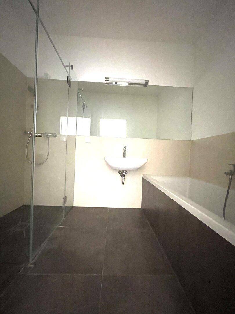 Modernes Badezimmer mit dunklen Fliesen, begehbarer Dusche, Badewanne und hellem Waschtisch.
