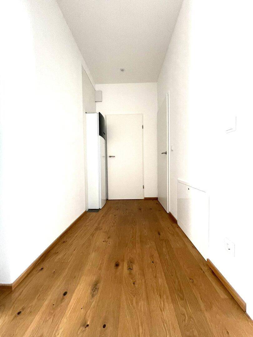 Langer Flur mit hellem Holzparkettboden und weißen Wänden, führt zu den verschiedenen Räumen.