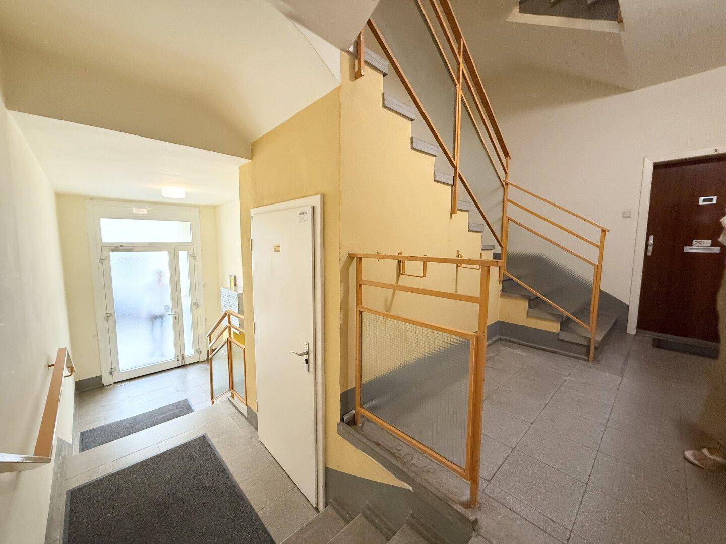Eingangsbereich und Treppenhaus eines Mehrfamilienhauses mit Fliesenboden und Handläufen.