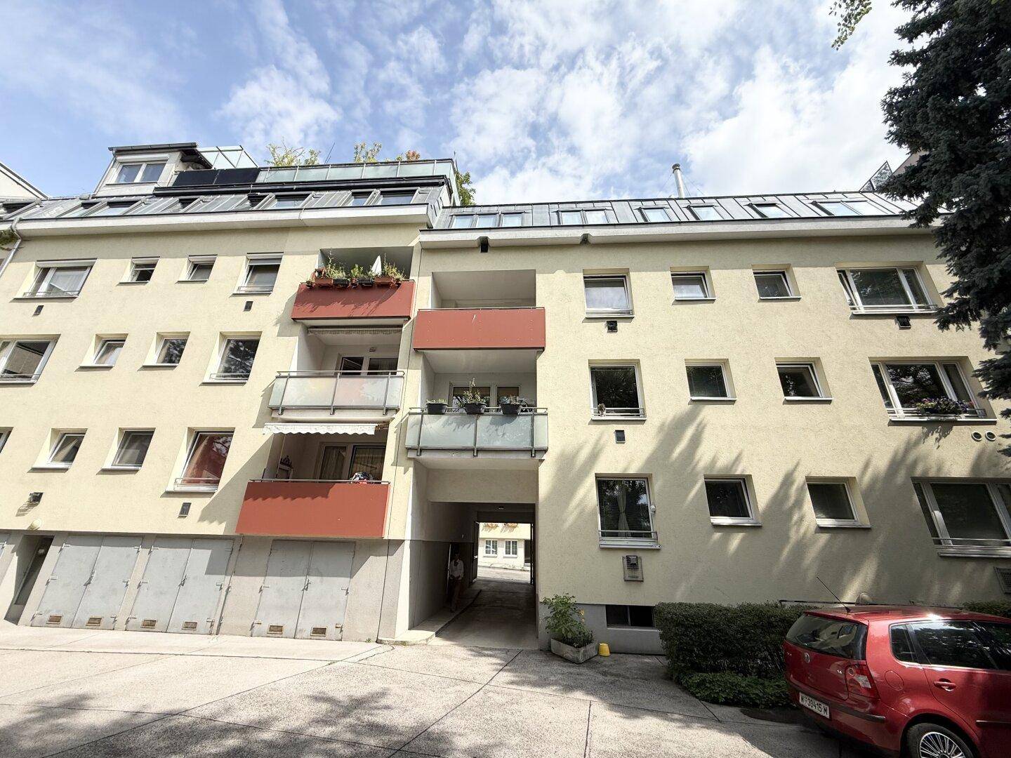 Ansicht des Mehrfamilienhauses mit Balkonen, vielen Fenstern und einem Durchgang zum Innenhof.