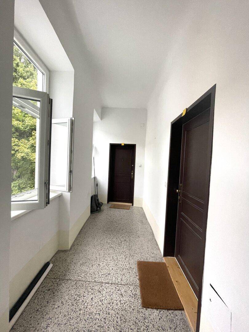 Heller Flur mit Terrazzoboden und Fenstern, die einen grünen Ausblick bieten.