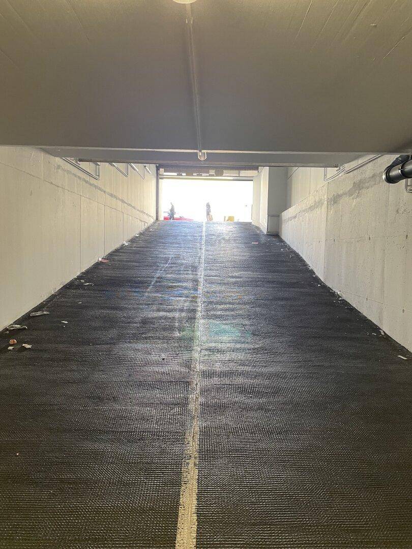 Einfahrt zu einer Tiefgarage mit einer breiten Rampe und strukturiertem Bodenbelag.