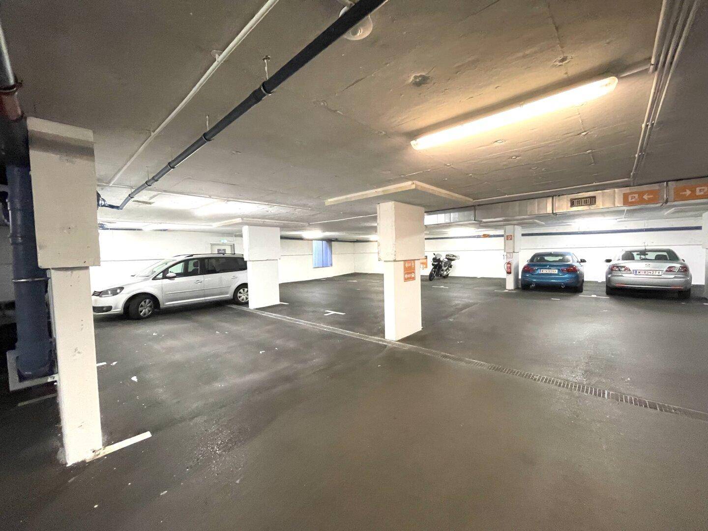 Geräumige Tiefgarage mit markierten Parkplätzen, Säulen und Beleuchtung, mehrere Fahrzeuge sind geparkt.