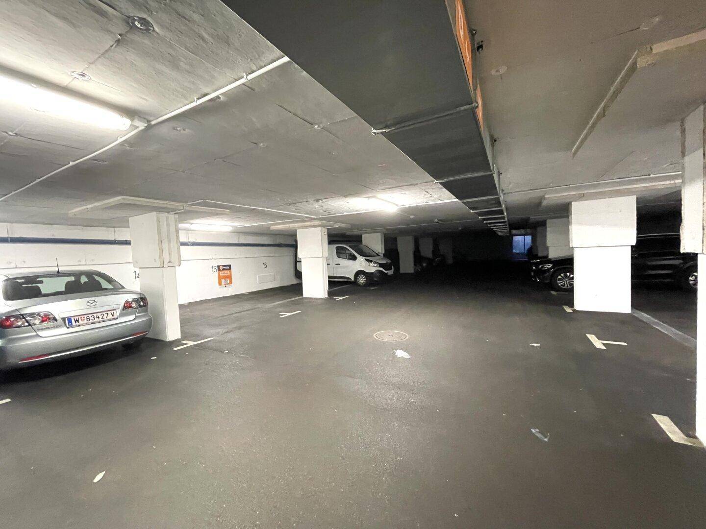 Weitere Ansicht der Tiefgarage mit zahlreichen Parkplätzen, Säulen und Deckenbeleuchtung, einige Autos sind abgestellt.