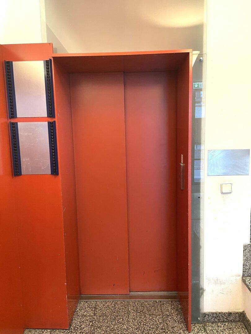 Roter Aufzug in einem Flur oder Eingangsbereich, bereit zur Benutzung.
