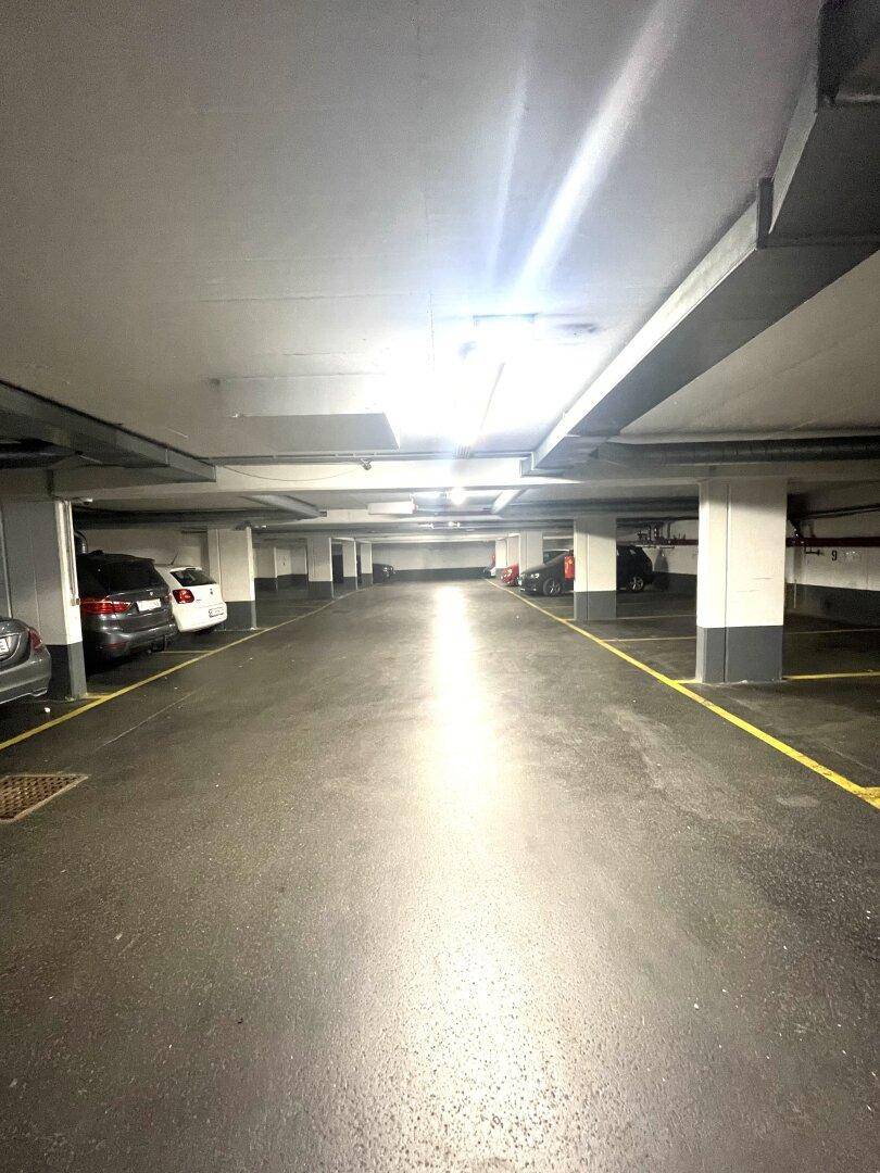 Weitläufige Tiefgarage mit zahlreichen Stellplätzen und heller Deckenbeleuchtung.