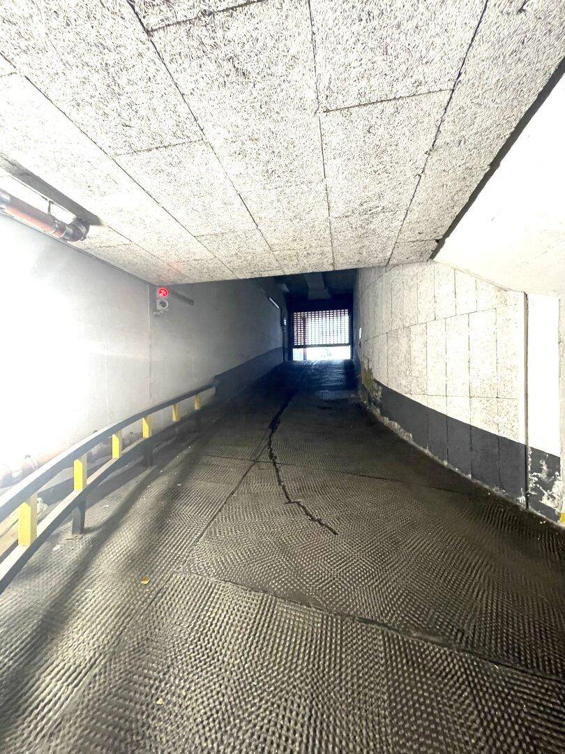 Abfahrtrampe, die in eine Tiefgarage führt, mit strukturiertem Boden und Beleuchtung.