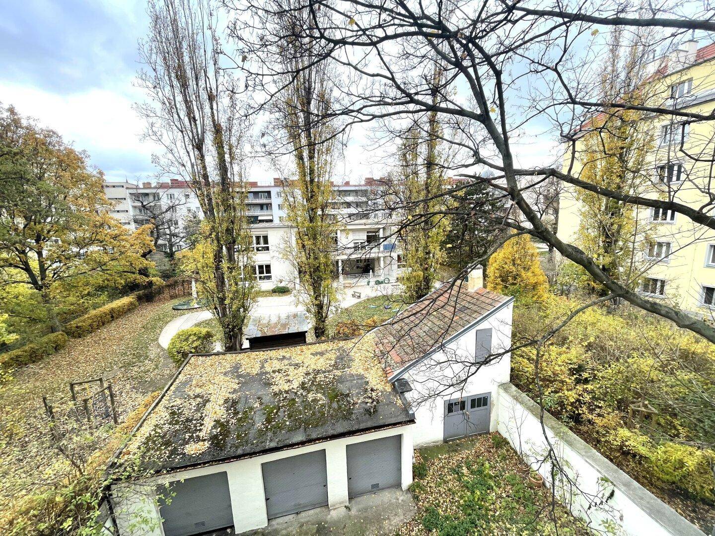 Blick auf einen Hinterhof mit Garagen und Bäumen im Herbstlaub.