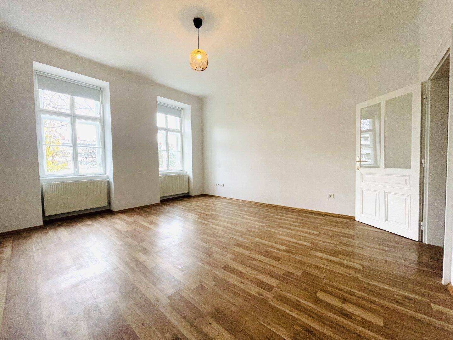 Geräumiges Zimmer mit Holzboden, hohen Decken und einer geöffneten Tür.