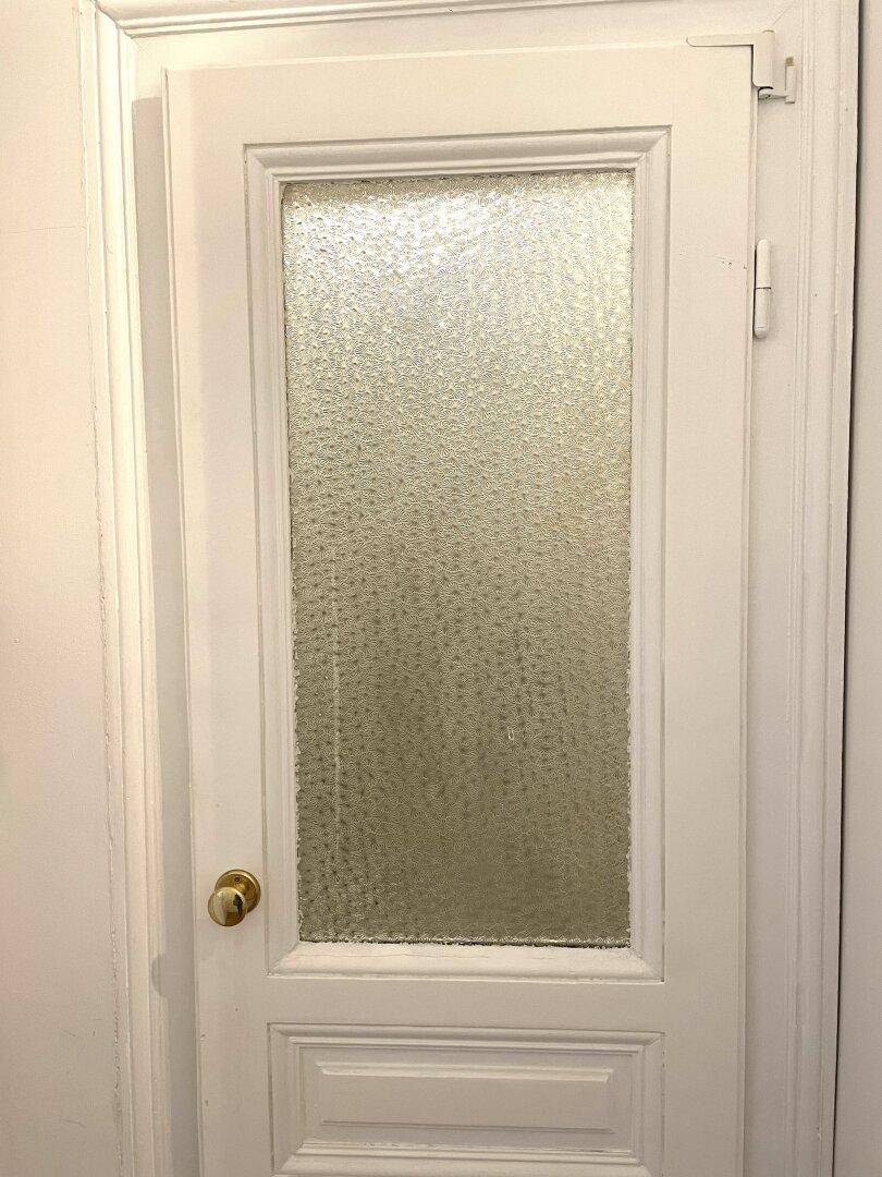 Nahaufnahme einer weißen Tür mit Milchglas und goldener Klinke.