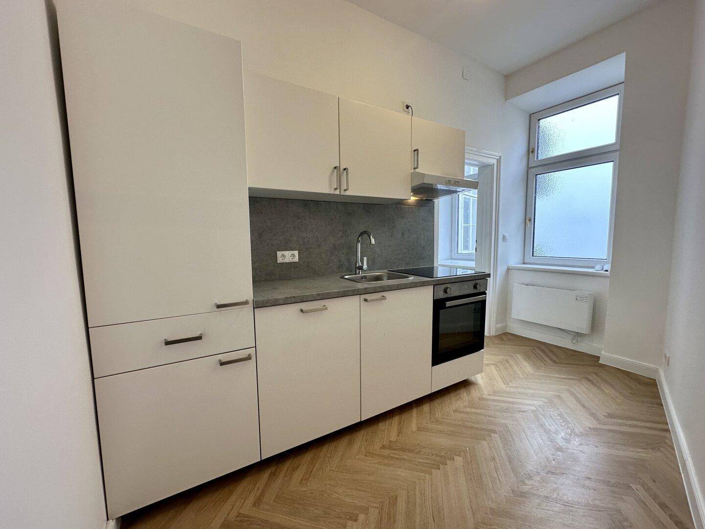 Moderne Küchenzeile mit weißen Schränken, integriertem Backofen und Fischgrätparkett.