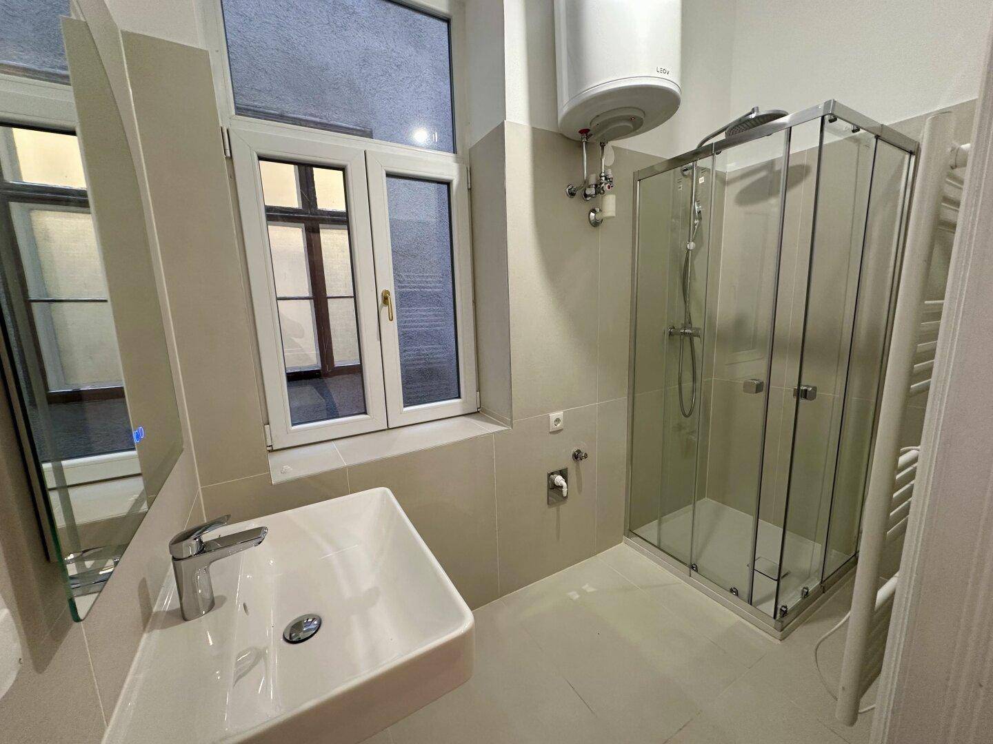 Helles Badezimmer mit Glasduschkabine, modernem Waschbecken und beigen Wandfliesen.