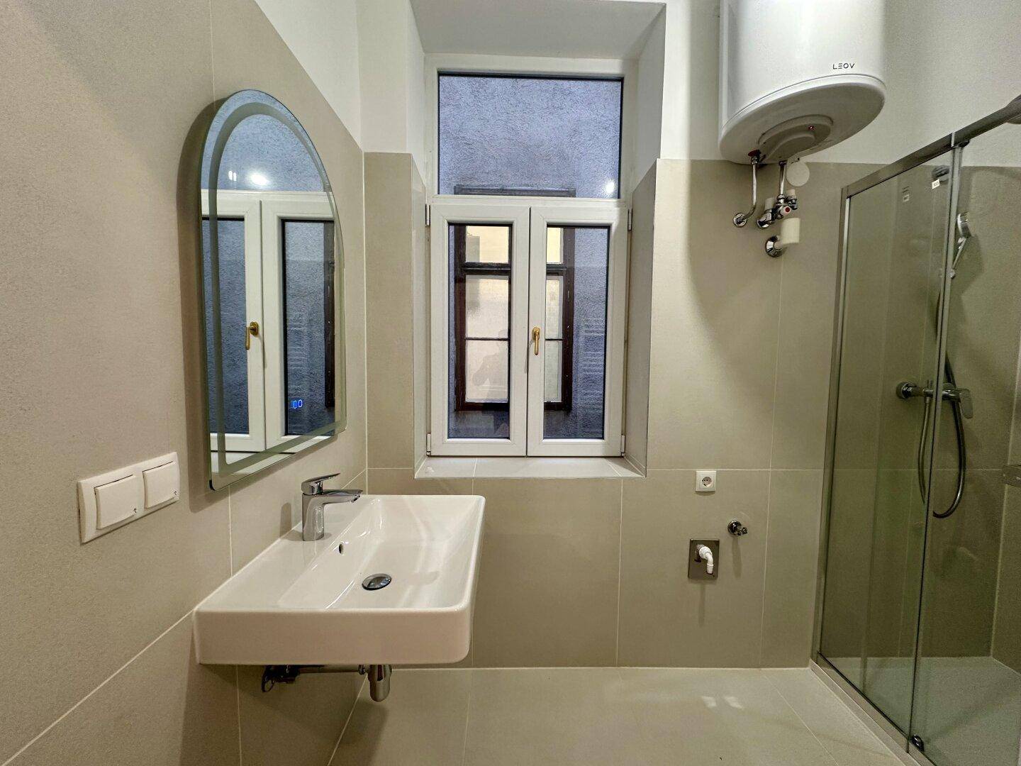 Modernes Badezimmer mit beigen Fliesen, Duschkabine und einem Fenster für Tageslicht.