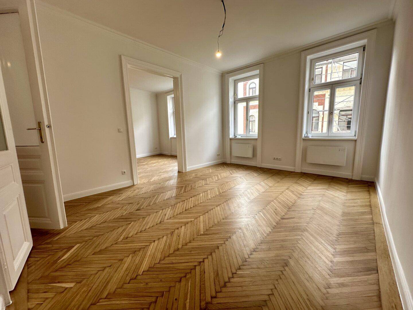 Geräumiges Zimmer mit klassischem Fischgrätparkett und Blick auf die Straße.