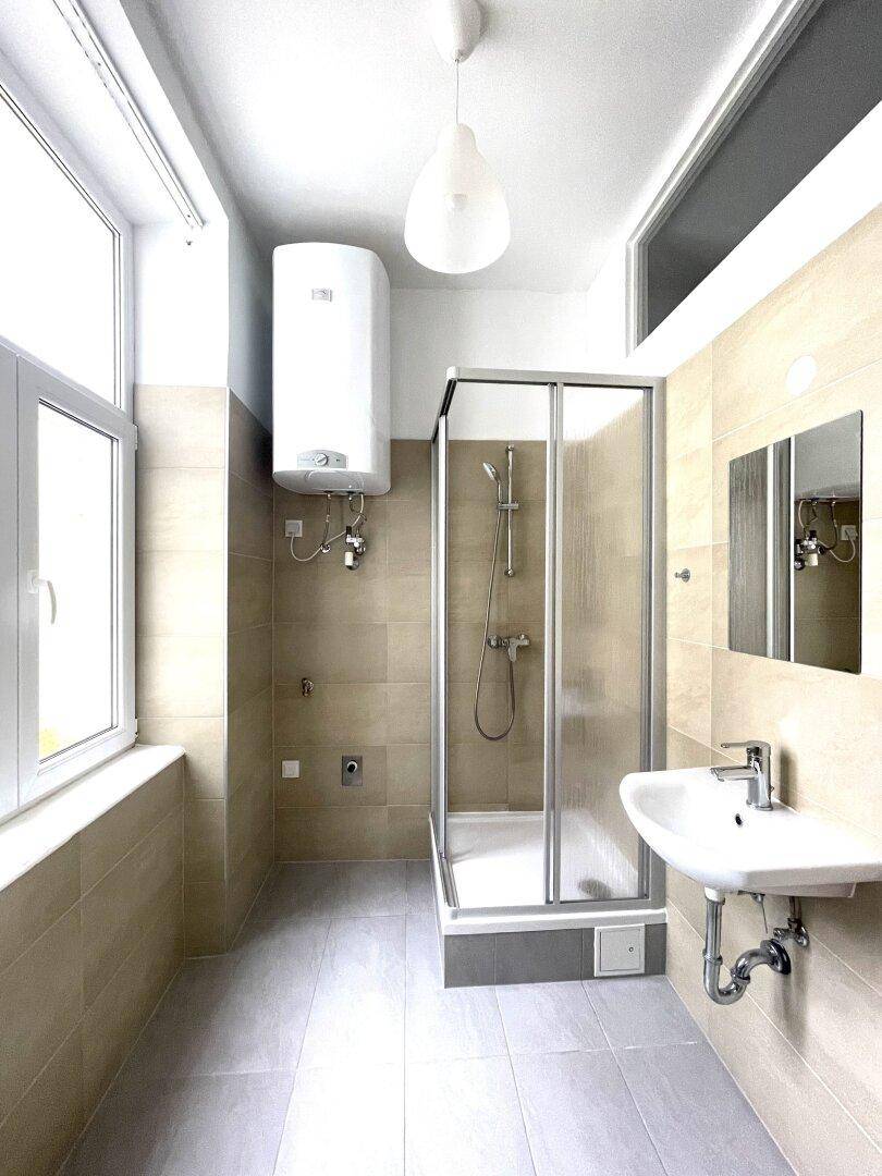 Modernes Badezimmer mit Duschkabine, Waschbecken, Warmwasserboiler und Fenster für Tageslicht.