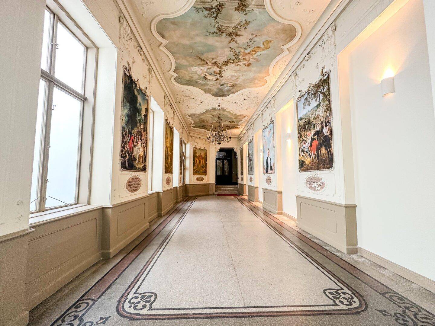 Langer, eleganter Flur mit aufwendigen Decken- und Wandmalereien sowie gemustertem Steinboden.