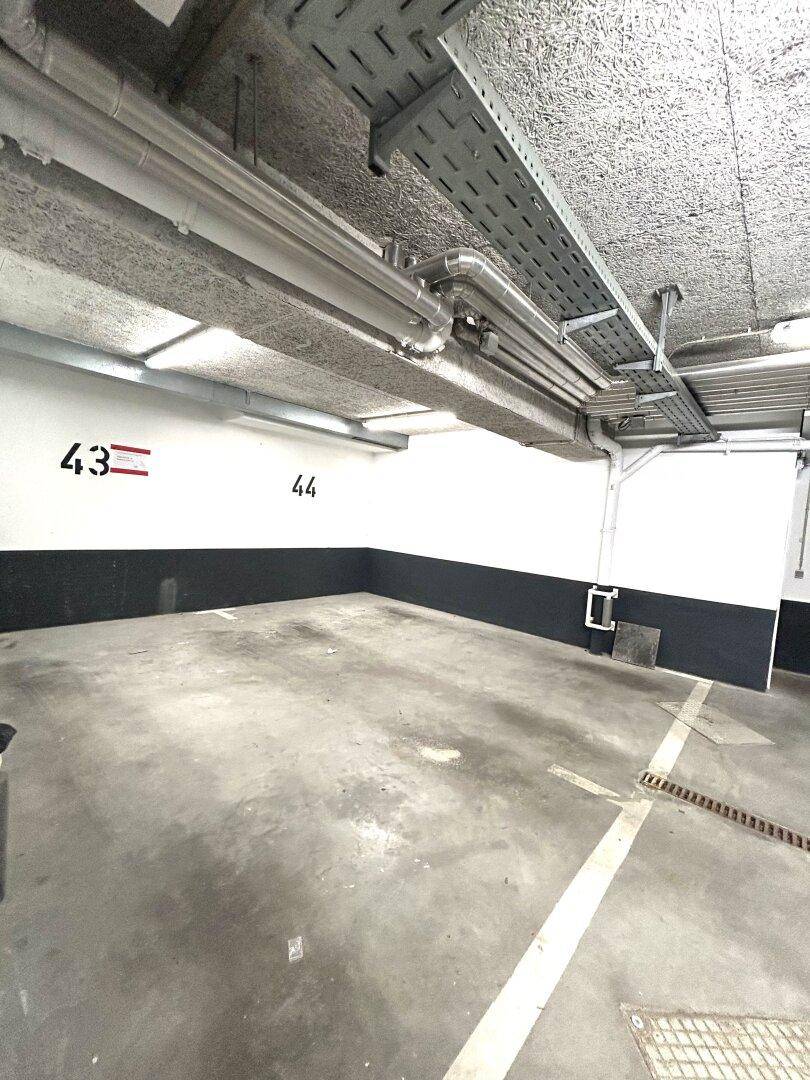 Tiefgarage mit freiliegenden Leitungen und markierten Stellplätzen.