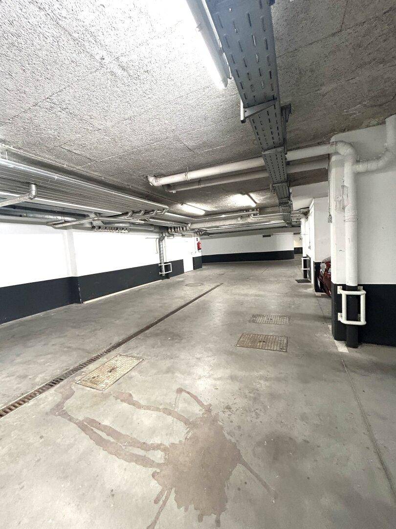 Geräumige Tiefgarage mit Betonboden und sichtbaren Installationen an der Decke.