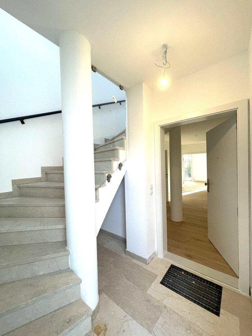 Eingangsbereich mit Steinfliesenboden und einer eleganten Treppe mit modernem Geländer.