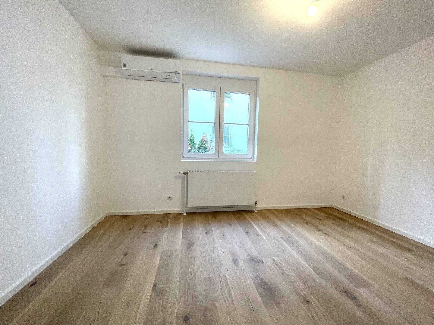 Helles Schlafzimmer mit Holzboden, Fenster und installierter Klimaanlage für Komfort.