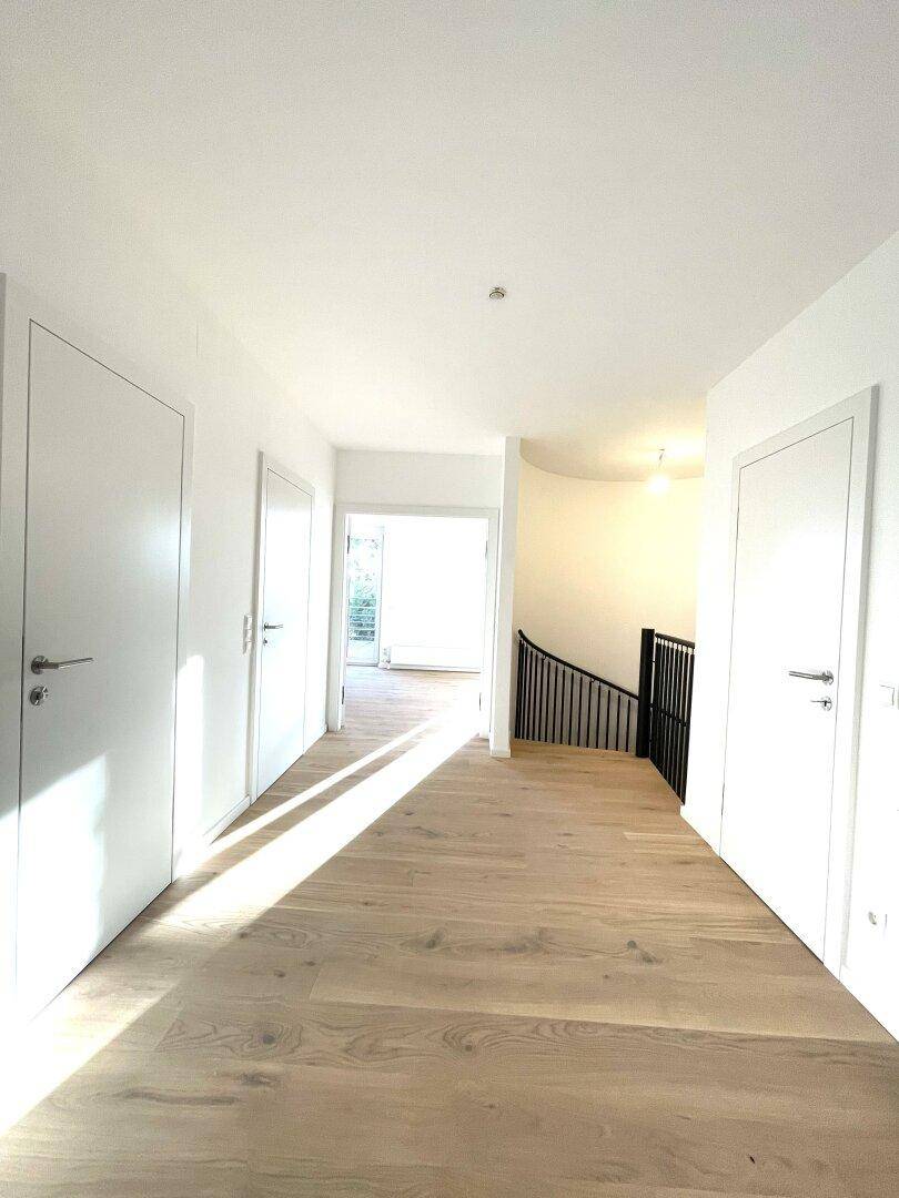 Heller Flur mit Holzboden, weißen Türen und einem Blick auf die moderne Treppe im Hintergrund.