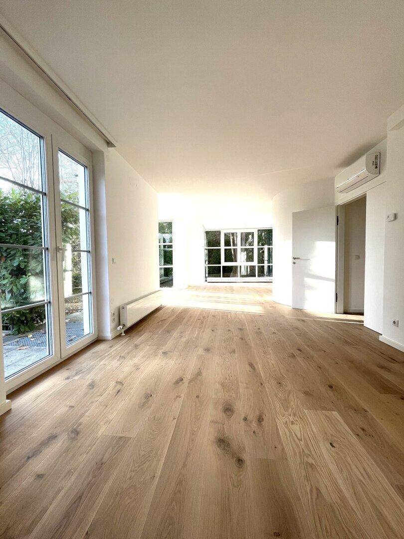 Langer, heller Wohnraum mit Holzboden, Klimaanlage und großen Fenstern für viel Licht.