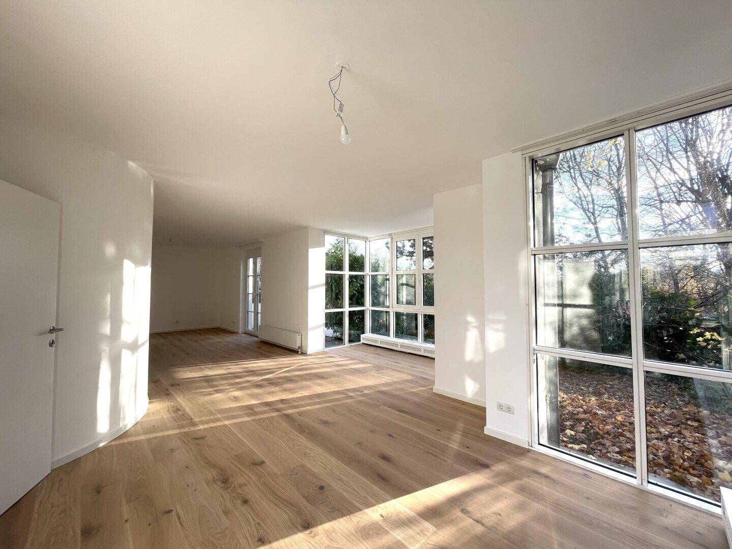 Lichtdurchfluteter Wohnraum mit elegantem Holzboden und weitem Blick durch die großen Fenster.