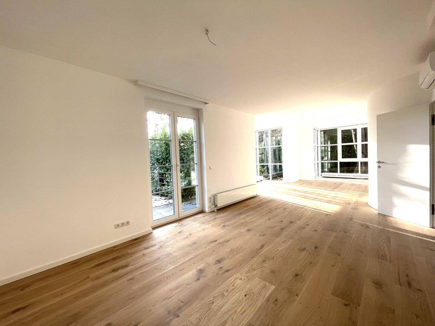 Geräumiger Wohnbereich mit Holzboden, großen Fenstertüren und Zugang zum Außenbereich.